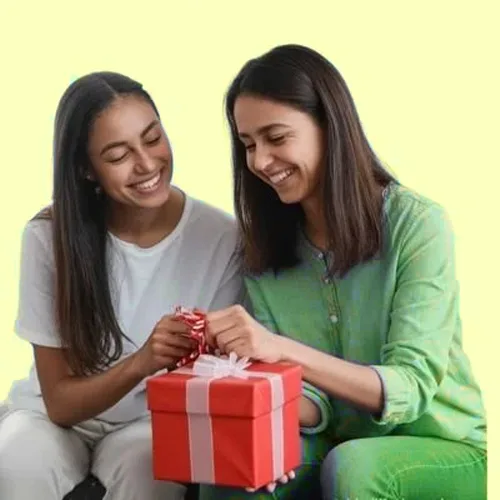 Two women smile as they unwrap a red gift box with a white ribbon together, seated against a pale yellow background.