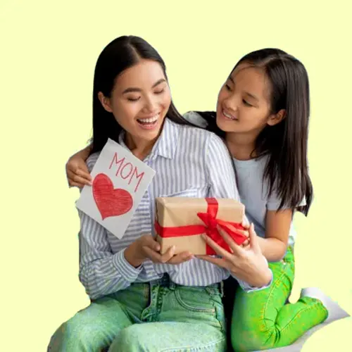 Two smiling girls give a small wrapped gift to their mom, sharing a card with a red heart.