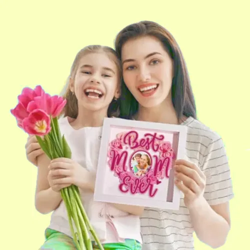 Mother and daughter smiling while holding pink tulips and a 'Best Mom Ever' card against a pale yellow background.