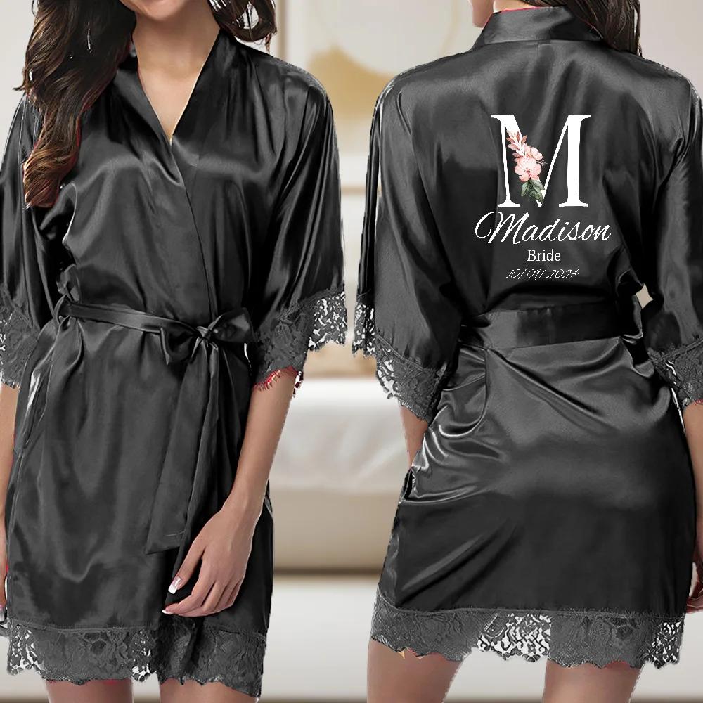 Black satin bridal robe with lace trim at the sleeves and hem, tied at the waist; back features a large white 'M' with a pink floral accent and the words 'Madison Bride' with a date underneath (10/01/2024).