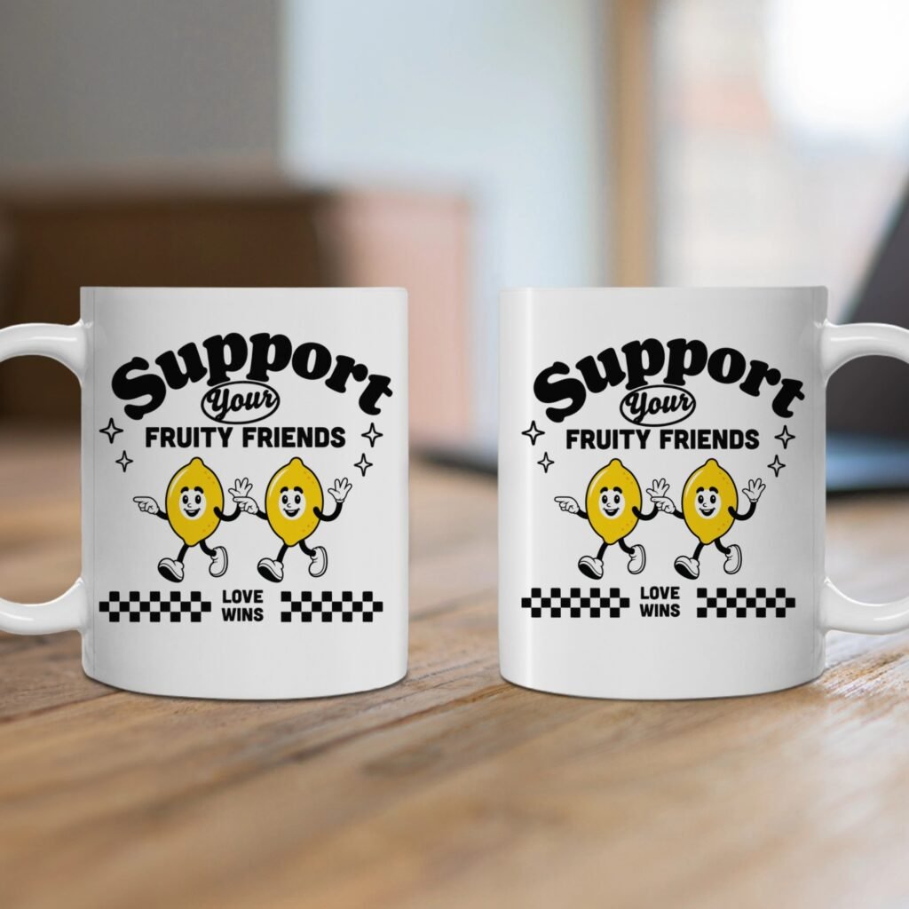 Two white mugs on a wooden table displaying a bold graphic that says 'Support Your Fruity Friends' with cartoon waving lemons underneath the text.