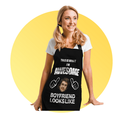 Smiling woman wearing a black novelty apron that says 'This is what an awesome boyfriend looks like' with thumbs-up icons, standing in front of a yellow circle background.