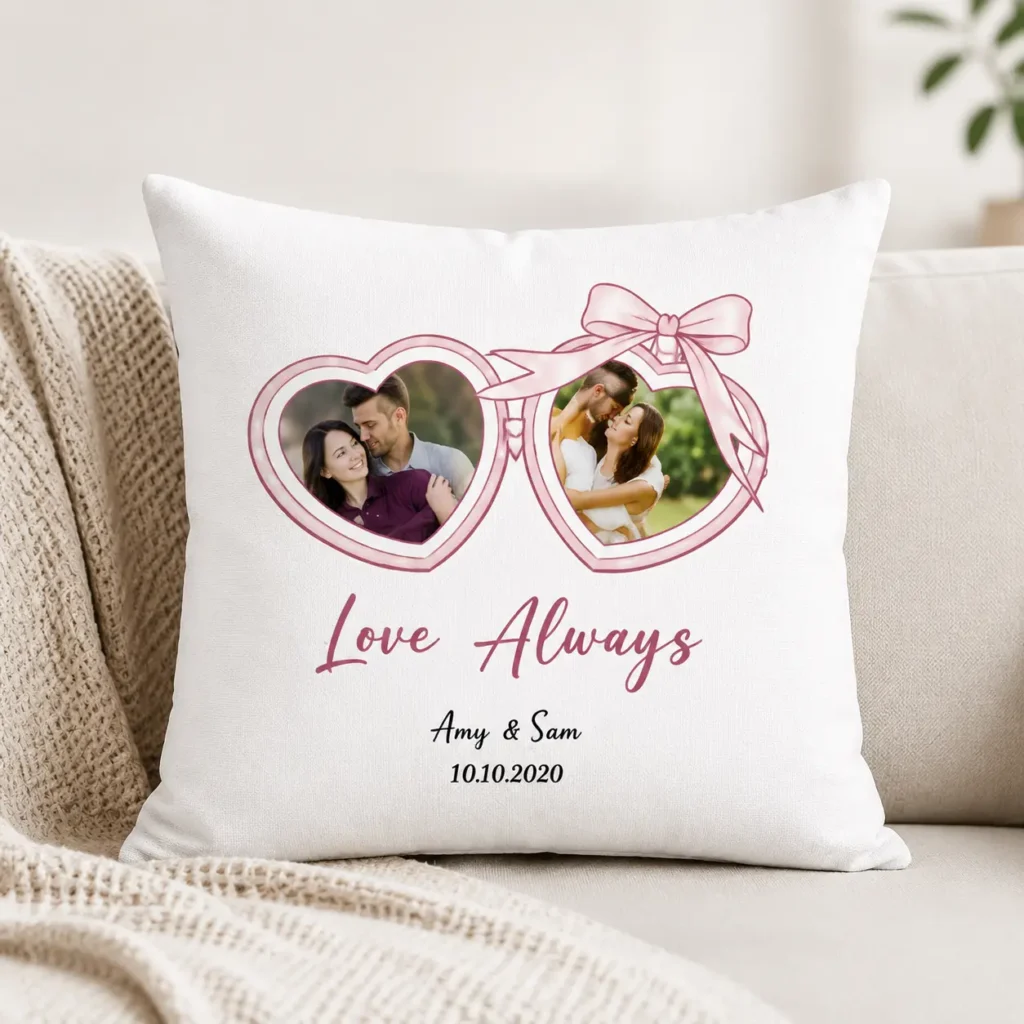 White decorative pillow with two pink heart-shaped frames holding couple photos, tied with a ribbon, and the words ‘Love Always’ with ‘Amy & Sam’ and ‘10.10.2020’