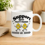 White mug with a cartoon of two smiling dancing lemons and the phrases 'Support your fruity friends' and 'Love Wins' with a black-and-white checkered border beneath.