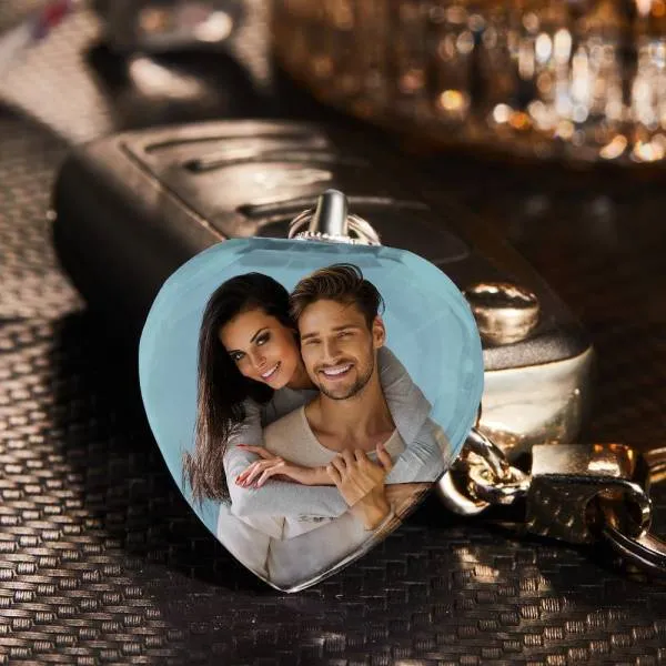 Heart-shaped photo keychain featuring a smiling couple, placed on a dark textured surface with a key ring nearby.