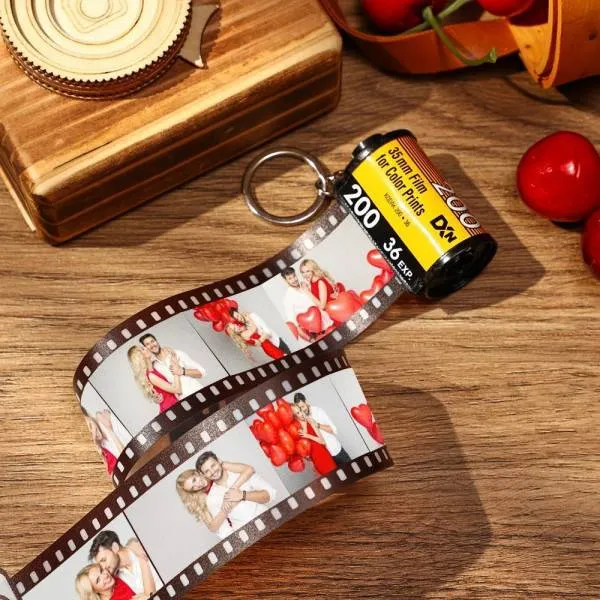 Film-strip keychain displaying a sequence of couple photos on a wooden table with a small box and cherries nearby.