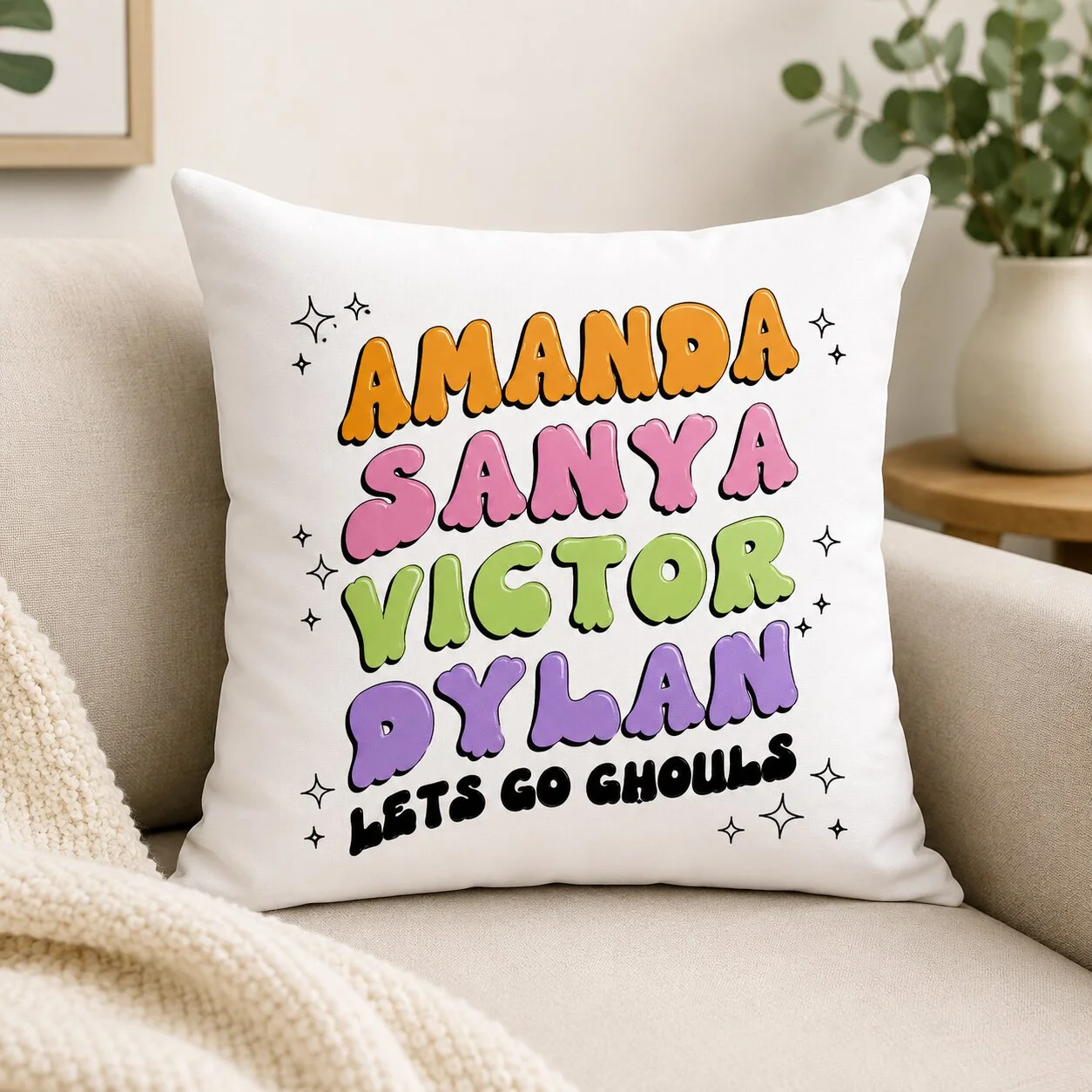 Square Pillow - Personalized Gifts For All Occasions Gift Supplier White pillow with colorful, cartoon-style names: AMANDA, SANYA, VICTOR, AXYLAN; phrase LET'S GO GHOULS in black at bottom with small stars around (fun, playful print). But the text reads 'Amanda Sanya Victor PXLan' as stylized letters.