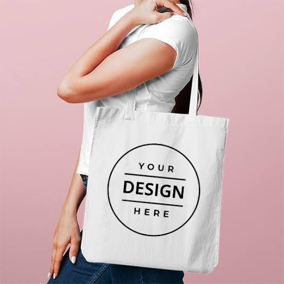 Tote Bag - Personalized Gifts For All Occasions Gift Supplier Person wearing a white shirt carries a white tote bag with a circular 'Your Design Here' logo against a pink background.