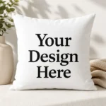 White decorative pillow with bold black text 'Your Design Here' on white fabric. A plant vase is nearby.