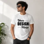 Man wearing a white T‑shirt with 'Your Design Here' in bold black letters, standing indoors in sunglasses, with a plant in the background.
